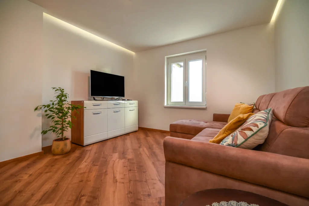 Open-plan living room with TV and sofa bed next to modern kitchen at SEDAMI apartment in Maribor with street and garden view
